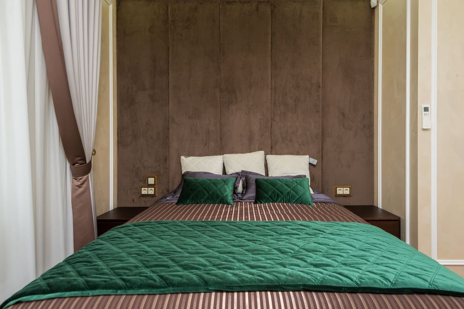 Lit double avec couvre-lit vert et coussins dans une chambre aux murs bruns capitonnés
