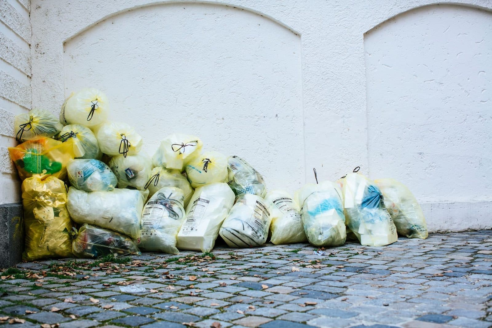 Stapel gelber Müllsäcke an einer weißen Wand auf dem Kopfsteinpflaster einer Stadtstraße