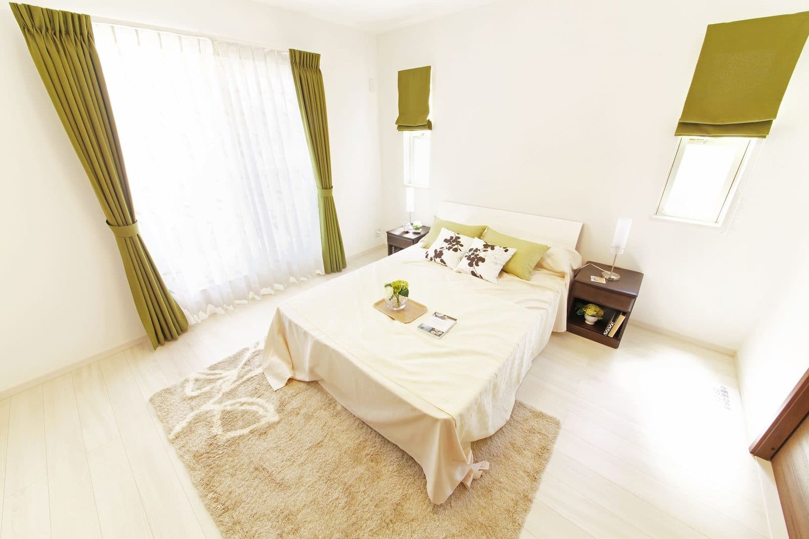 Chambre lumineuse avec lit double, draps blancs, tapis beige et rideaux verts près d'une fenêtre