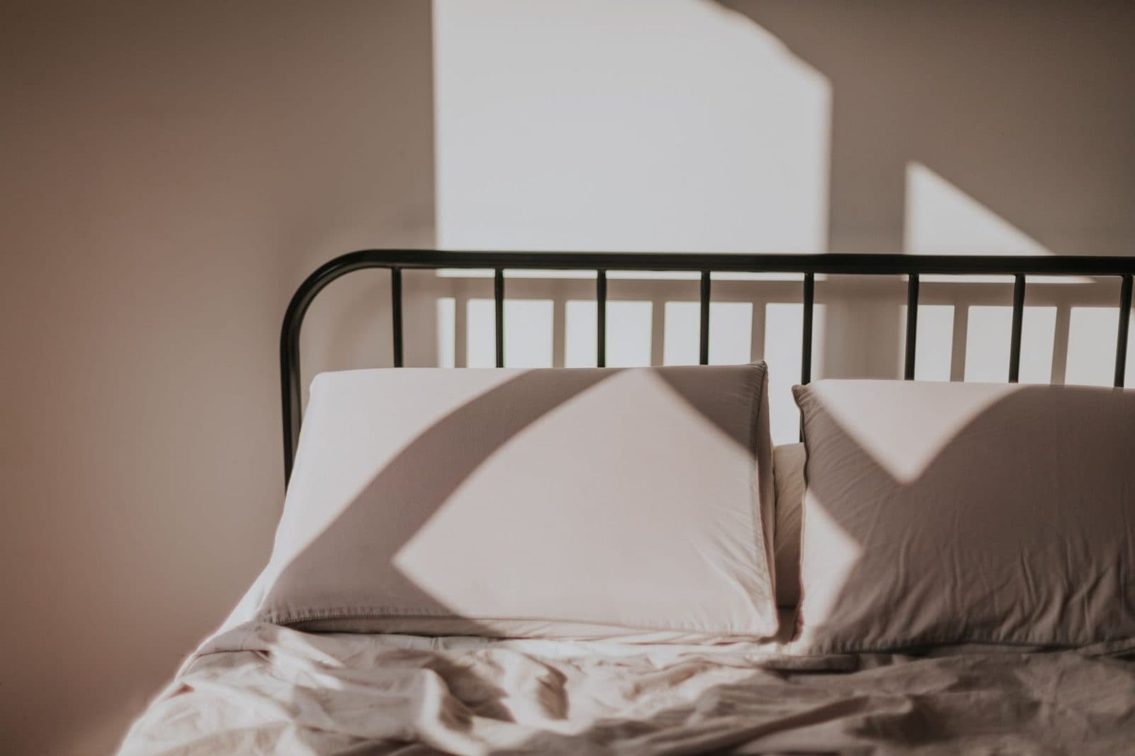 Lit en métal avec draps et oreillers clairs froissés dans une chambre baignée de lumière