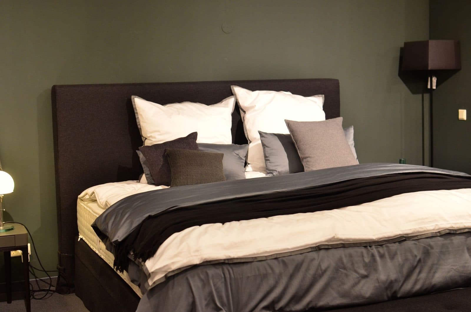 Lit double avec matelas, coussins et couette dans une chambre aux murs vert foncé