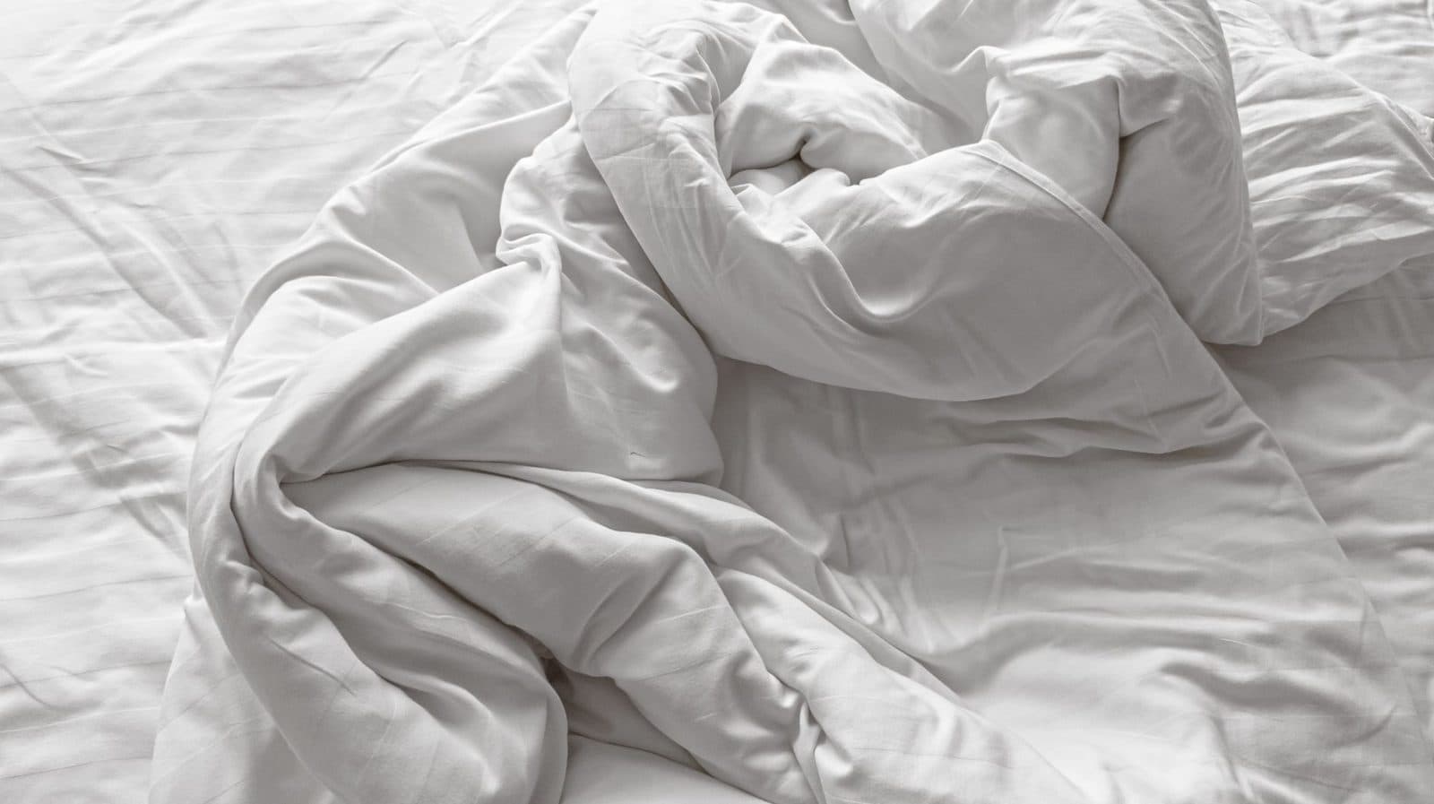 Letto disfatto con lenzuola e piumino bianchi stropicciati visti dall'alto