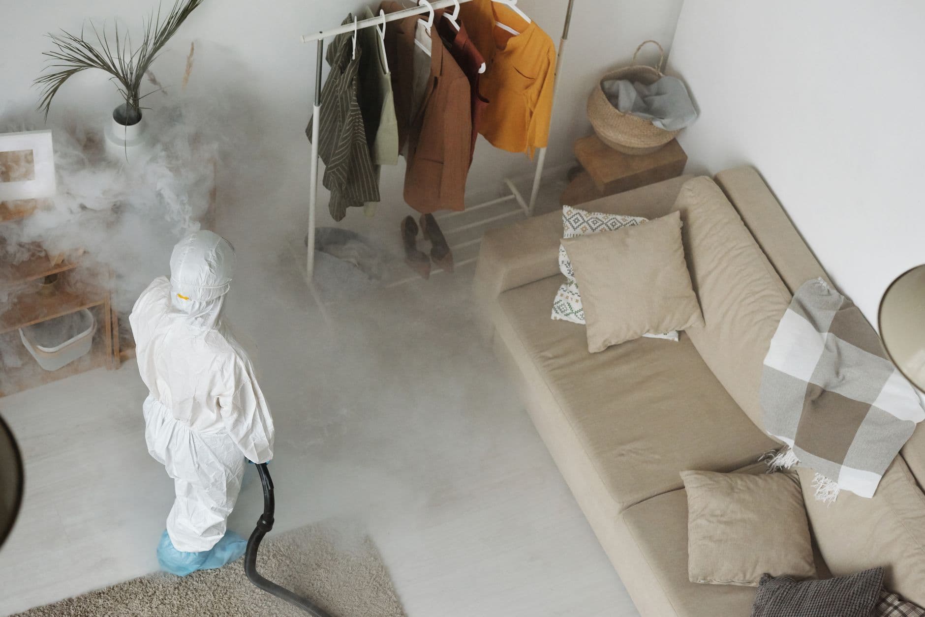 A person in a white protective suit dispersing disinsectization smoke in a living room.