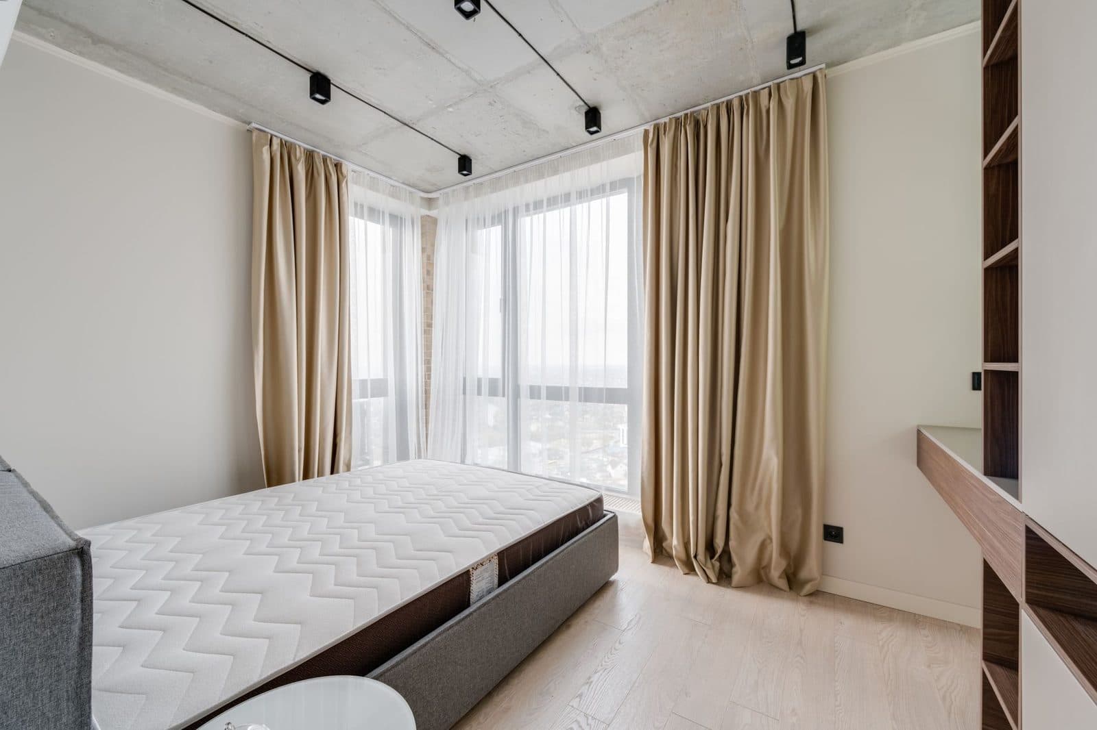 Bright bedroom with a bare mattress on the bed, beige curtains and light wood flooring