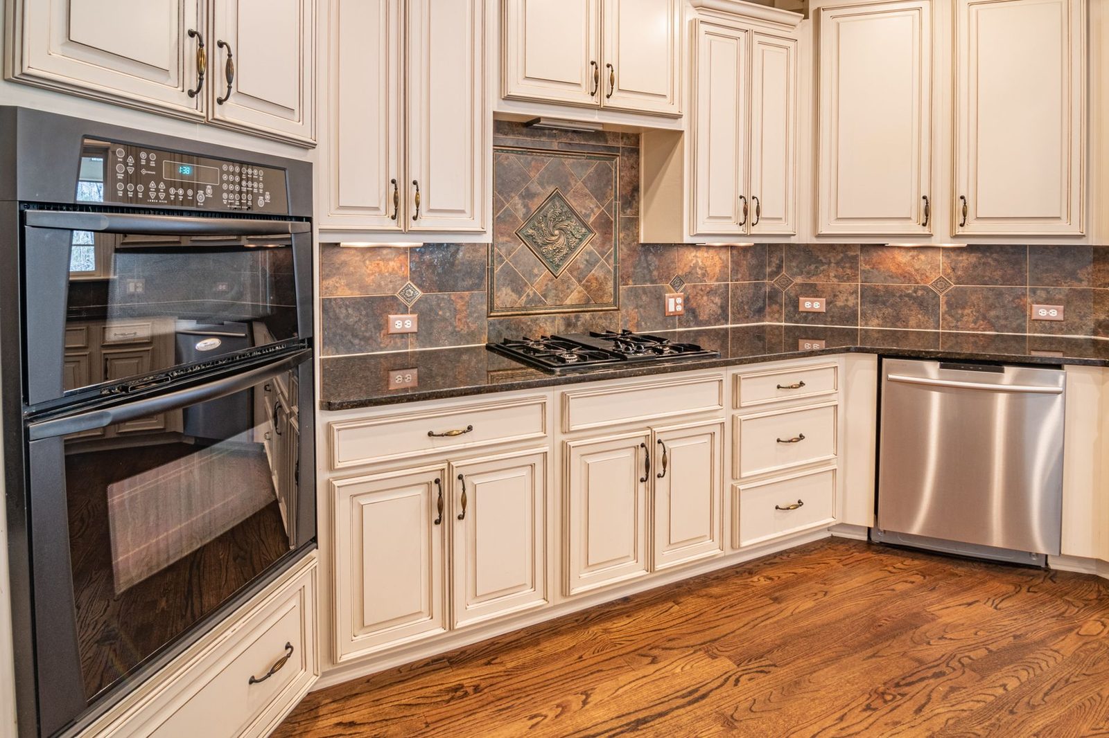 Cuisine équipée avec meubles blancs, plaque de cuisson, four encastré, lave-vaisselle et parquet en bois