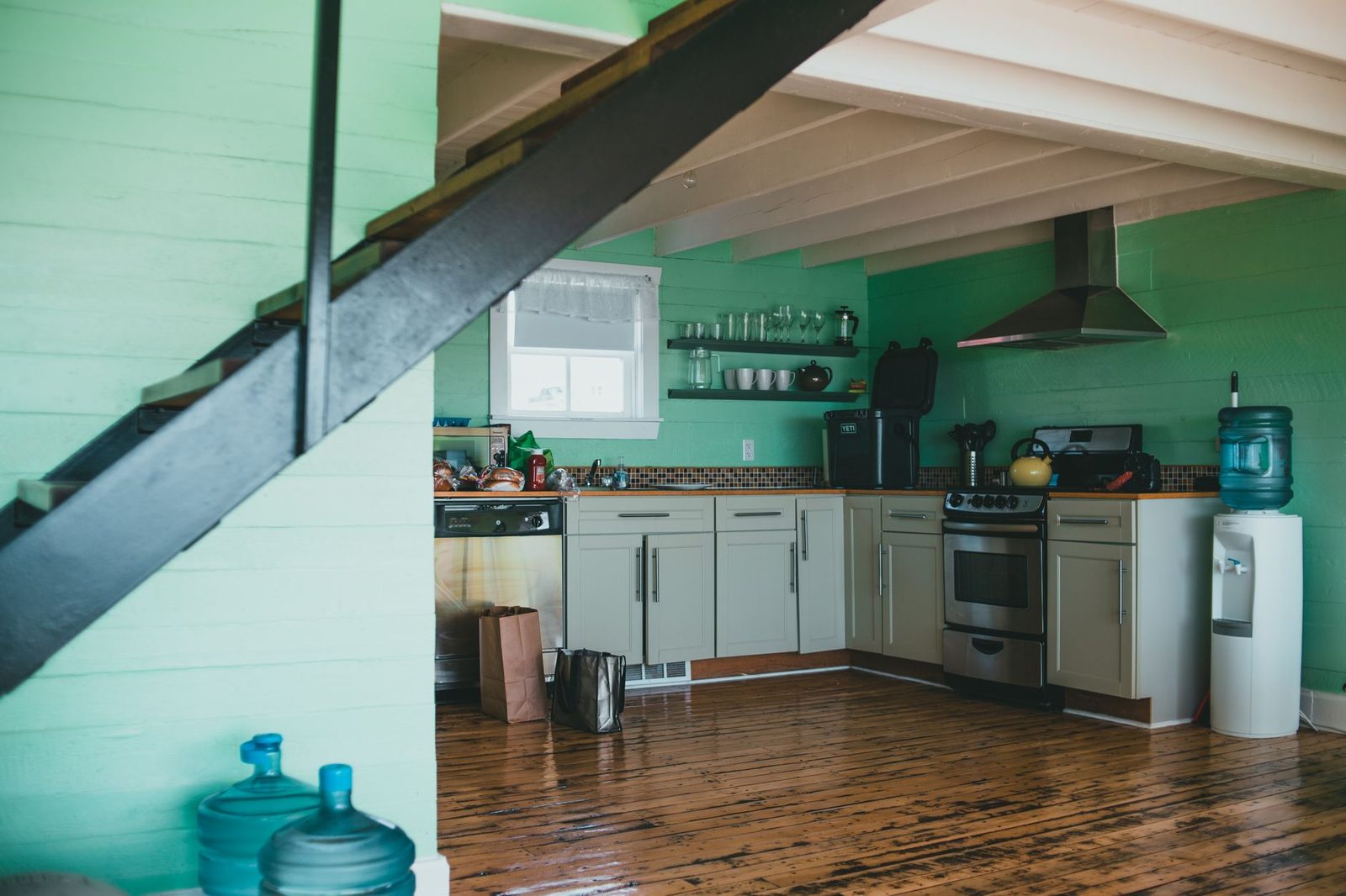Cuisine d'une maison aux murs verts avec parquet, gazinière, hotte et fontaine à eau