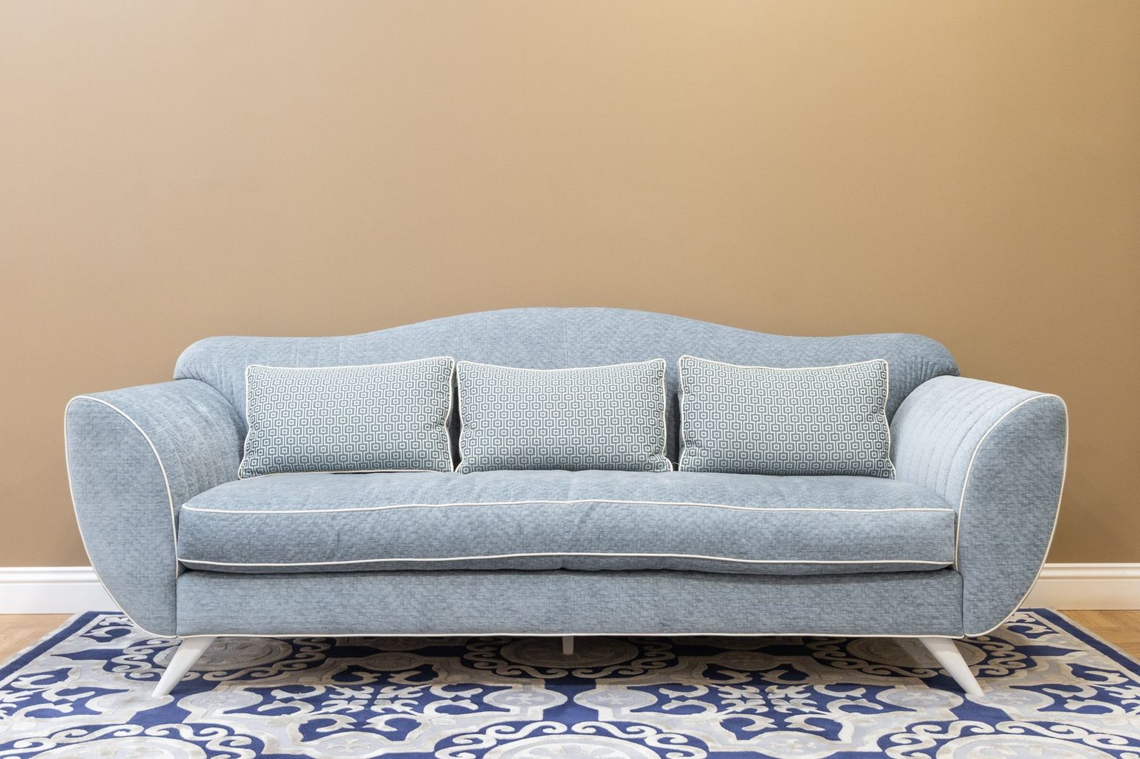 Canapé bleu clair avec coussins dans un salon, devant un mur beige et un tapis à motifs bleus