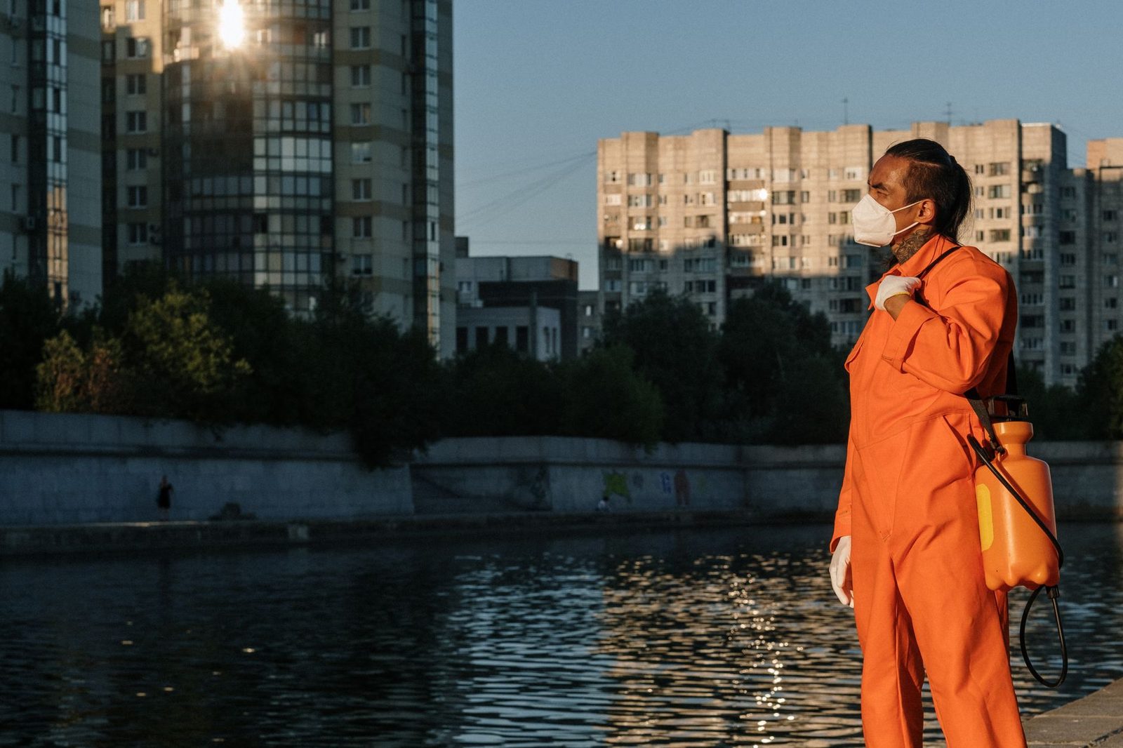 Technicien en combinaison orange et masque, pulvérisateur sur le dos, devant des immeubles d'habitation