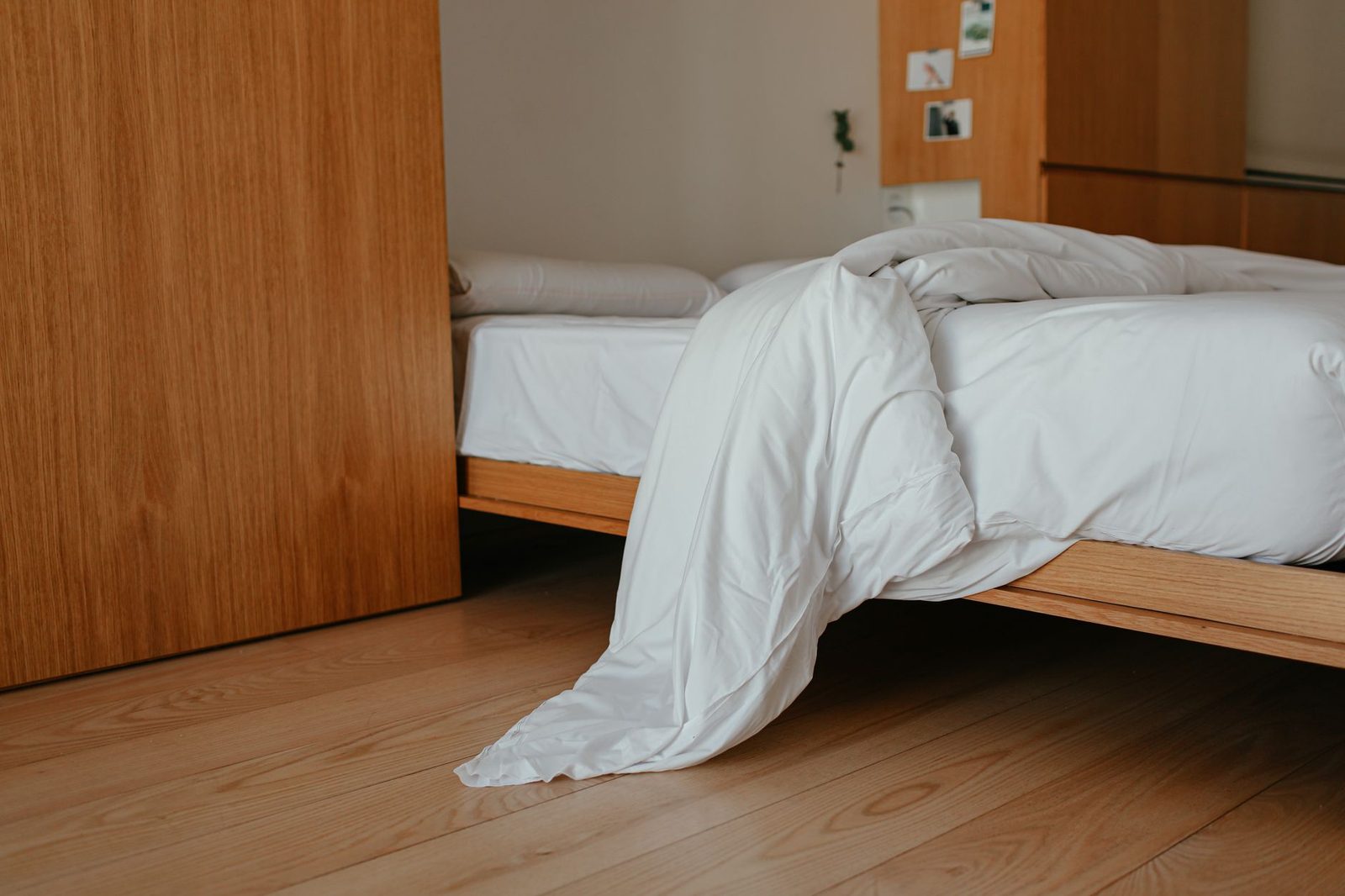 Lit en bois avec couette blanche défaite dans une chambre au parquet clair