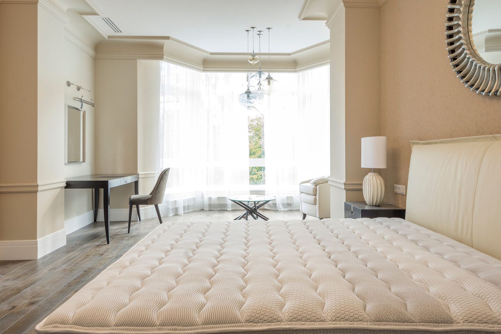 Matelas nu sans draps dans une chambre claire avec bureau, fauteuil et grande fenêtre voilée