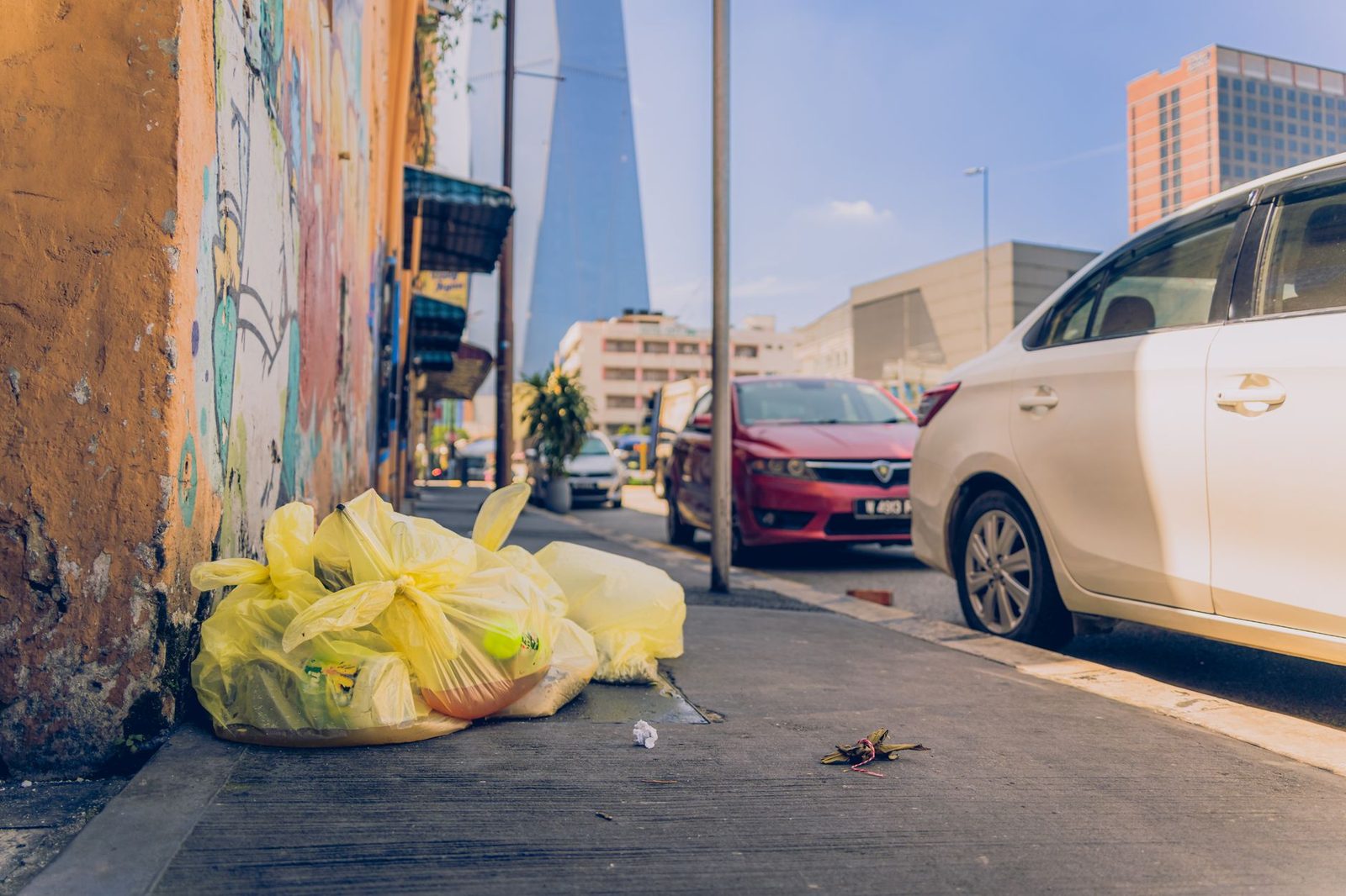 Gelbe Müllsäcke auf einem Gehweg entlang einer besprühten Mauer, geparkte Autos im Hintergrund