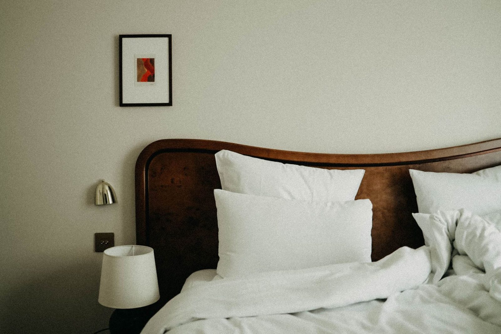 Lit avec tête de lit en bois, draps et oreillers blancs dans une chambre aux murs clairs