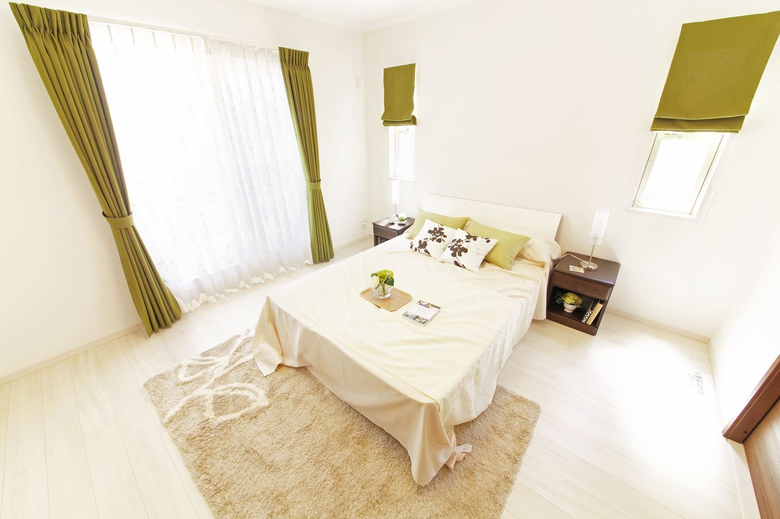 Chambre lumineuse avec lit double, draps blancs, tapis beige et rideaux verts près d'une fenêtre
