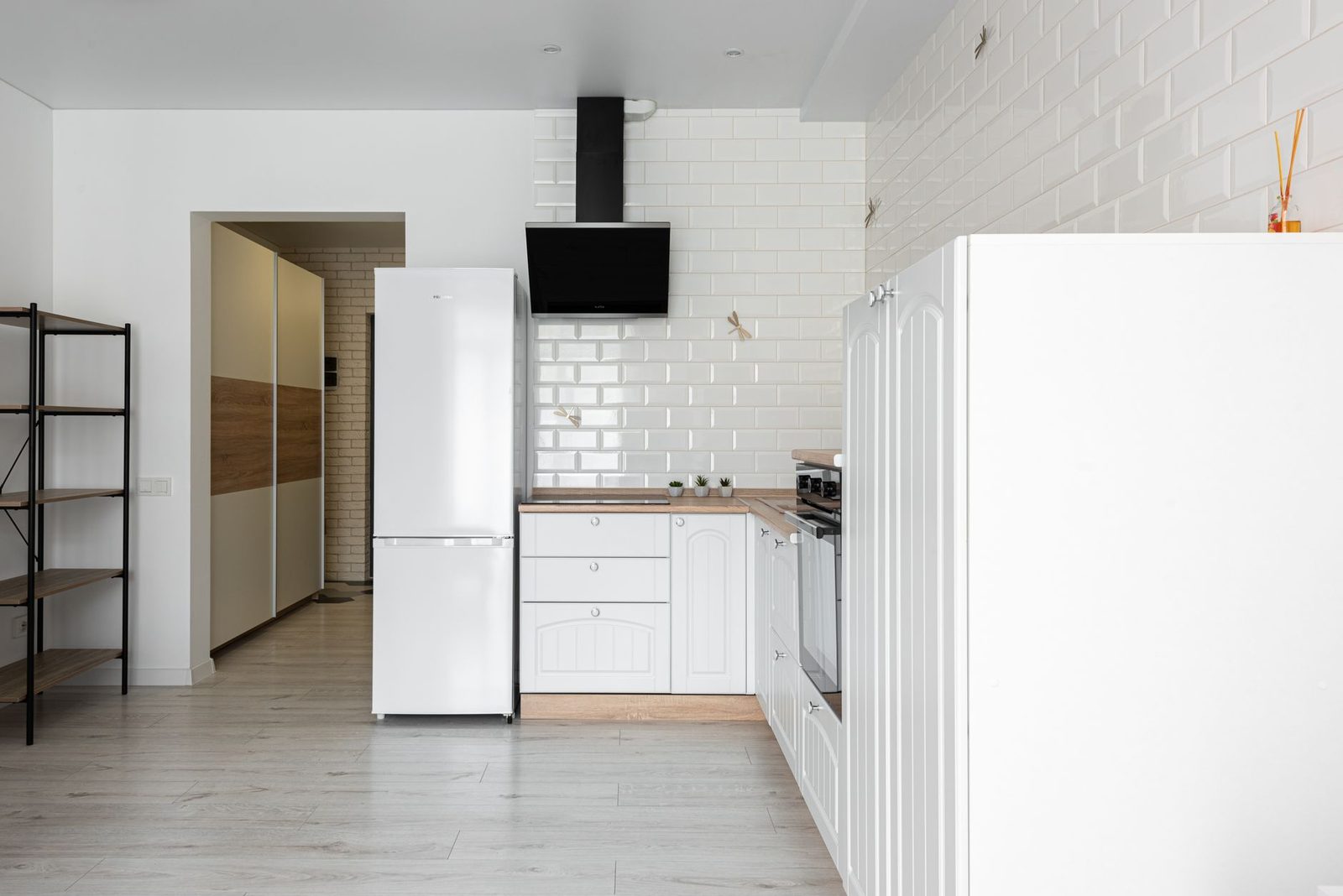 Cuisine blanche moderne avec réfrigérateur, hotte, carrelage métro et sol en parquet clair dans un logement