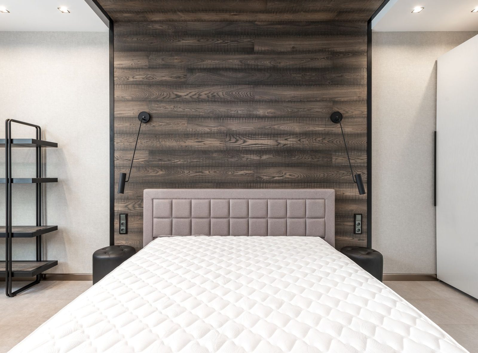 Cama de casal com colchão branco nu e cabeceira estofada num quarto com parede em madeira