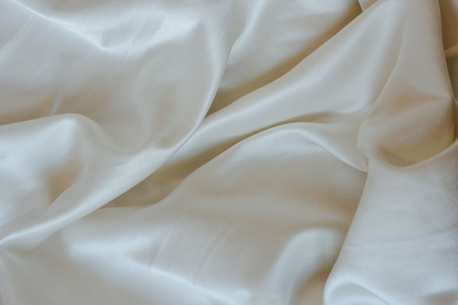 Lençol branco amarrotado sobre uma cama, grande plano do tecido acetinado e das suas pregas