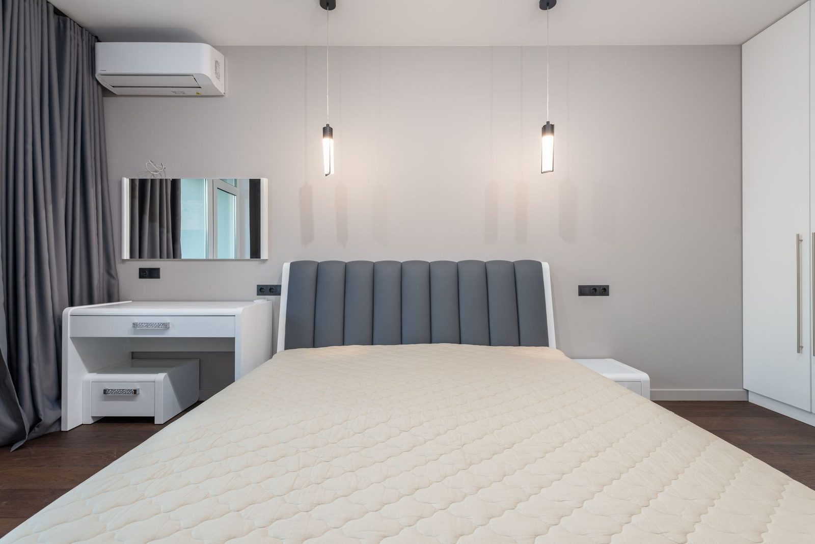 Dormitorio moderno con cama grande, cabecero gris, tocador blanco y lámparas de suspensión
