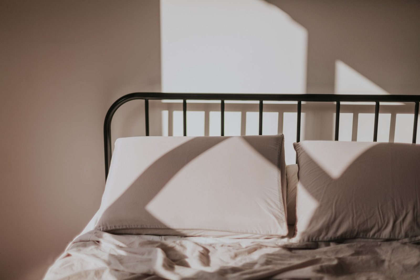 Lit en métal avec draps et oreillers clairs froissés dans une chambre baignée de lumière