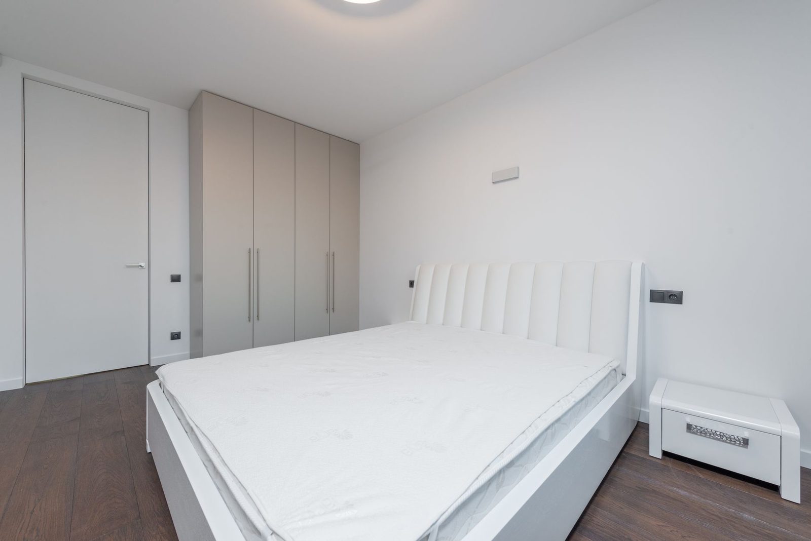 Chambre blanche épurée avec lit double, matelas nu, armoire et table de chevet