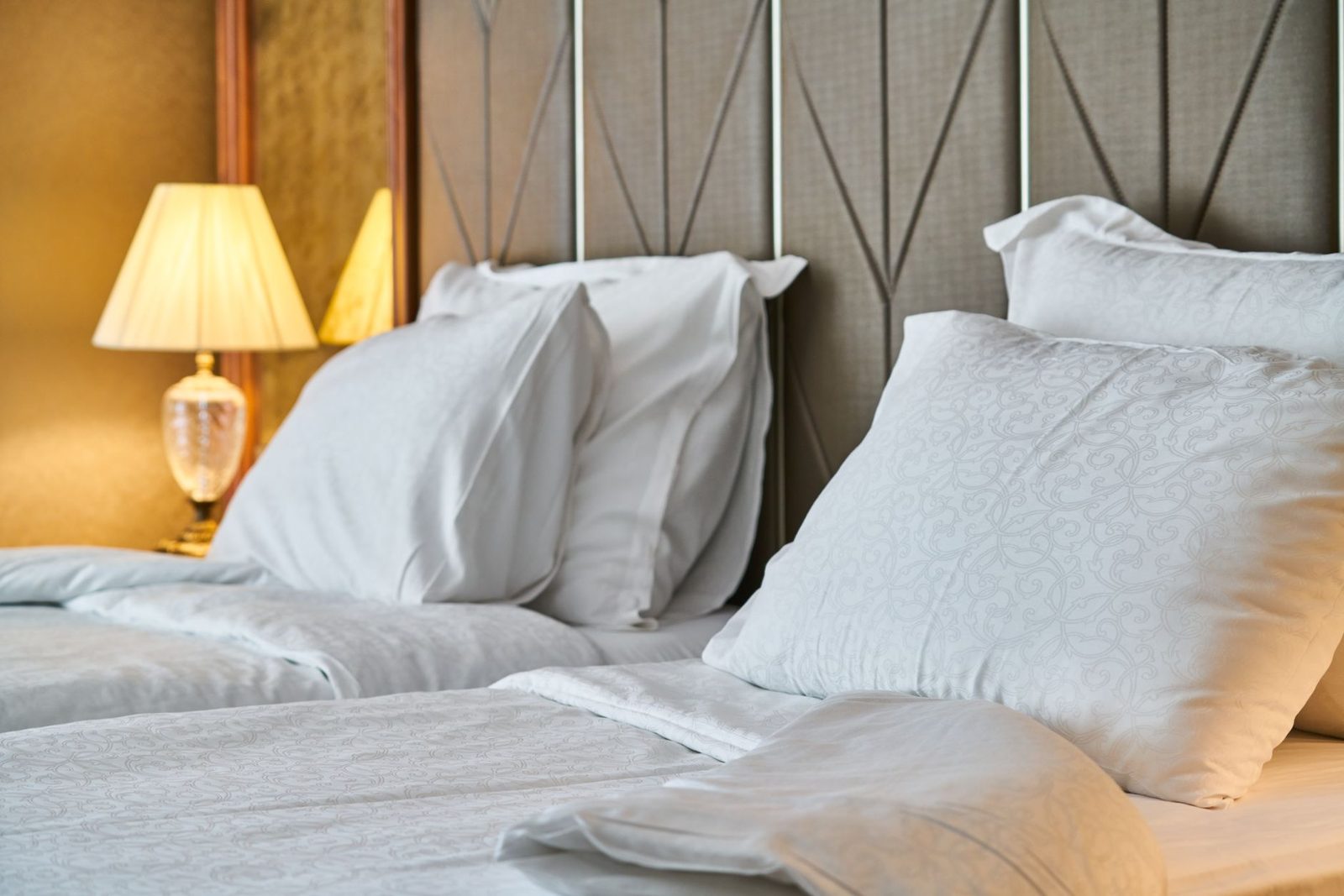 Bed met witte kussens en lakens voor een gecapitonneerd hoofdeinde, brandende nachtlamp
