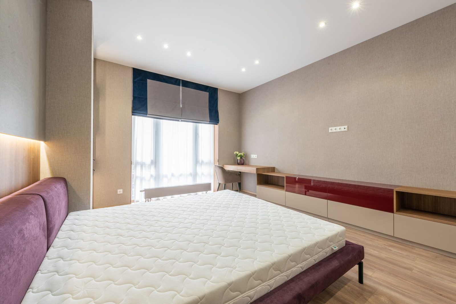Moderne slaapkamer met een bed waarvan de kale matras op een paarse boxspring ligt, bij een raam